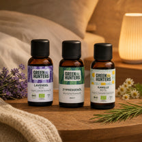 Ruhe & Schlaf Set mit Lavendel-, Zypressen- und Kamillenöl auf dem Nachttisch neben Lavendel und Kamillenblüten